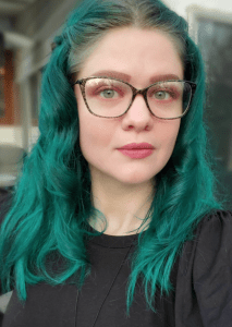 white woman with teal hair and glasses facing camera